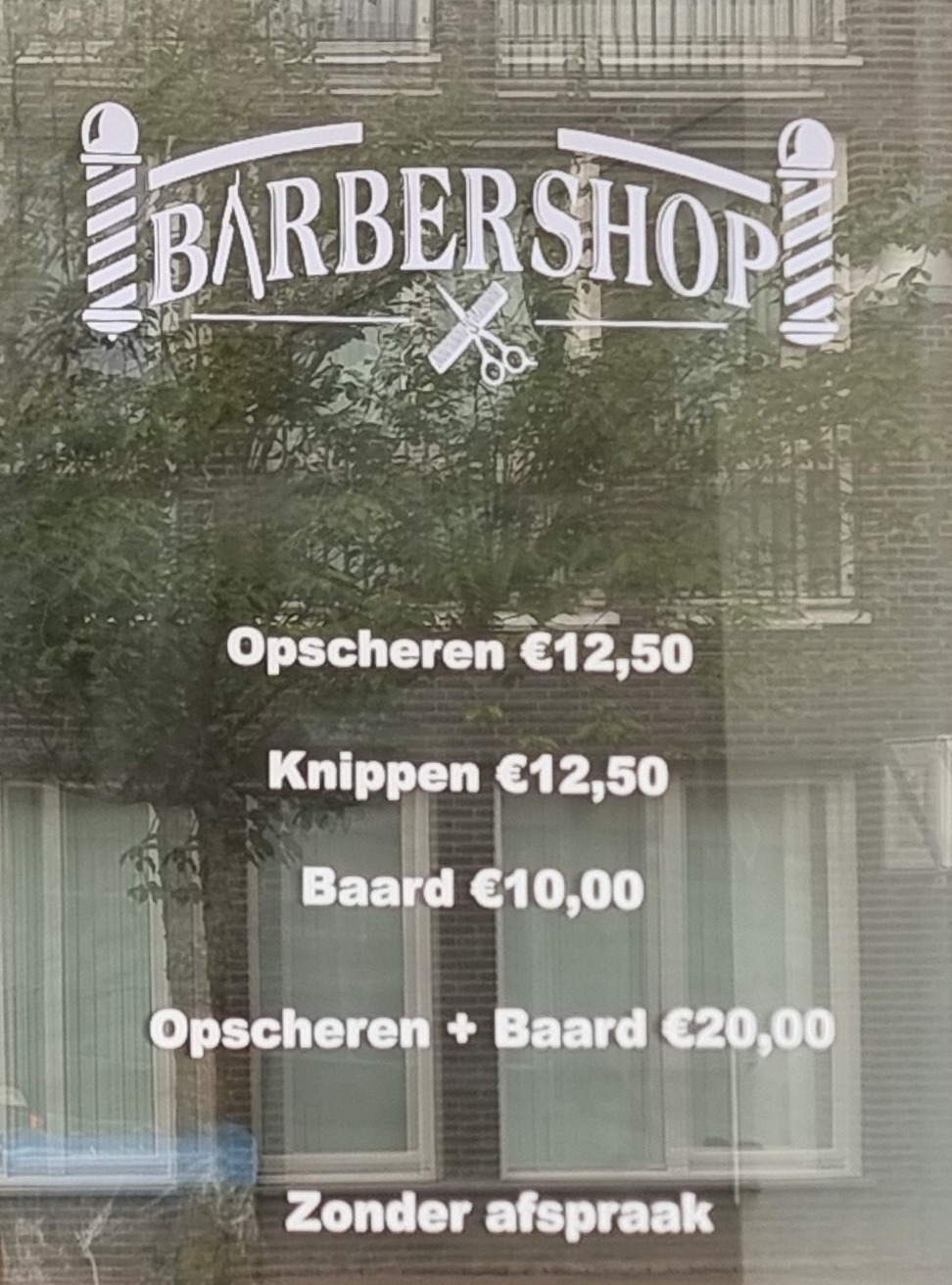 Het raam van Barbershop Mo met de prijslijst: opscheren, knippen, baard, zonder afspraak