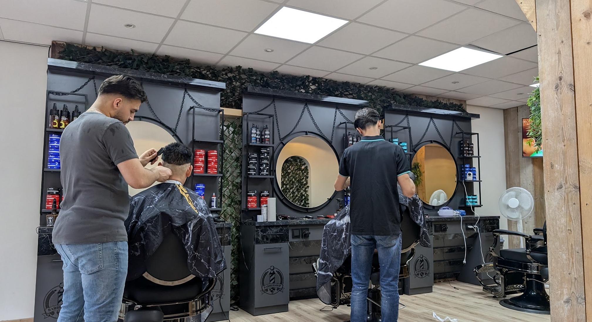 Twee kappers van Barbershop Mo aan het werk bij de ronde spiegels